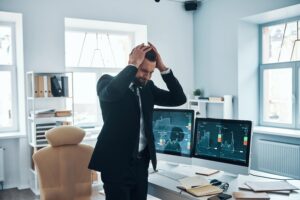 Frustrated man in office dealing with emotional stress while trading, representing why traders fail in Forex and Crypto: what most get wrong.