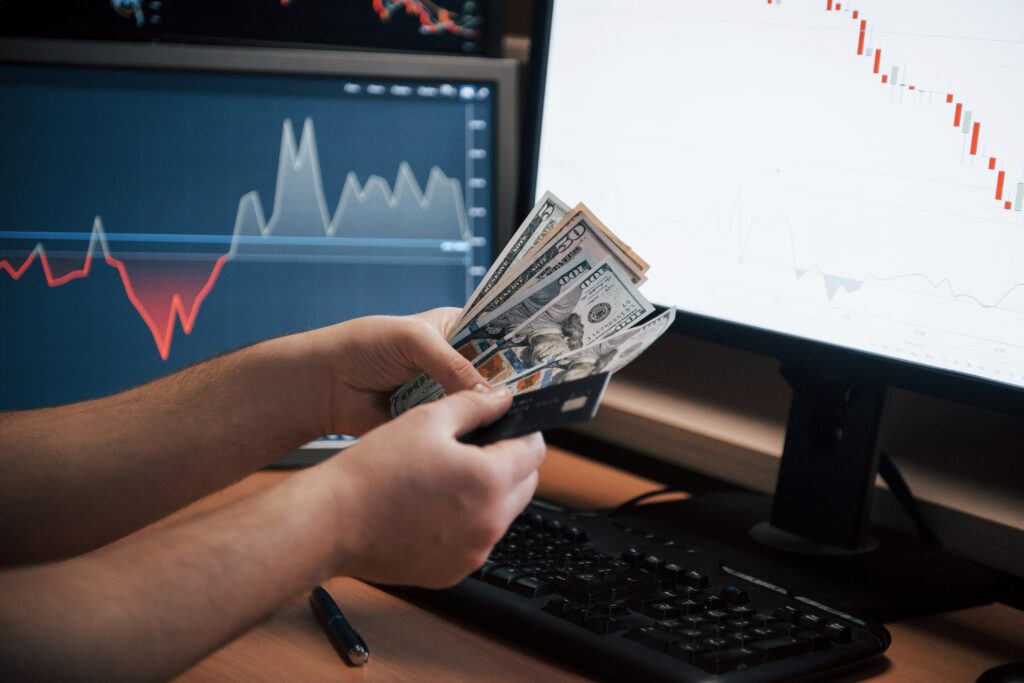 Hands holding money near trading screens showing forex managed account returns.