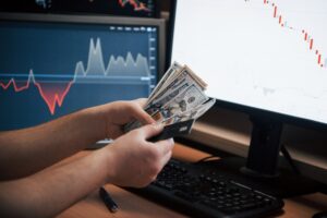 Hands holding money near trading screens showing forex managed account returns.