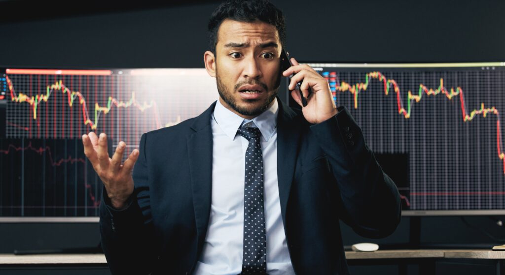 A man on the phone with a shocked expression, representing fear of loss in trading and trader anxiety.