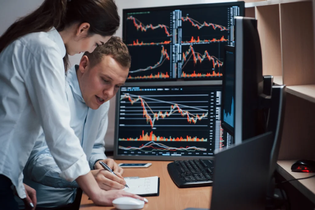 Two people in office analyzing copy trading with several market screens