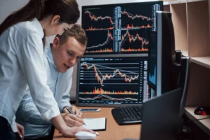 Two people in office analyzing copy trading with several market screens