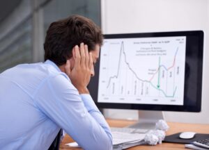 Rearview of a frustrated businessman at desk showing signs of Trading Stress in a high-pressure trading environment.