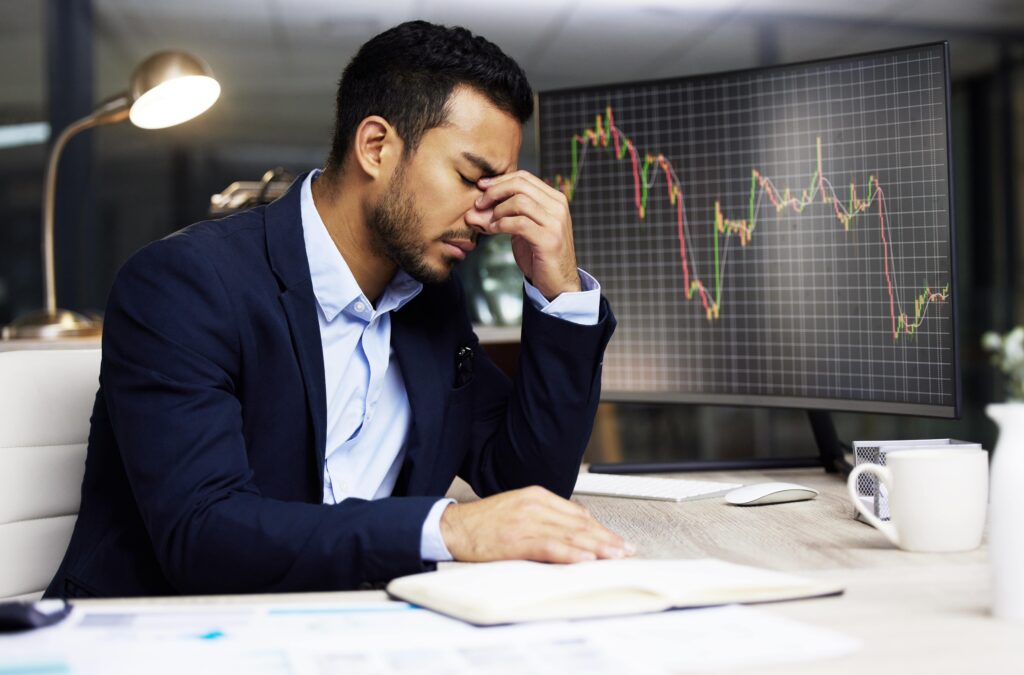 Trader stressed after a losing week in trading with falling market chart on screen.