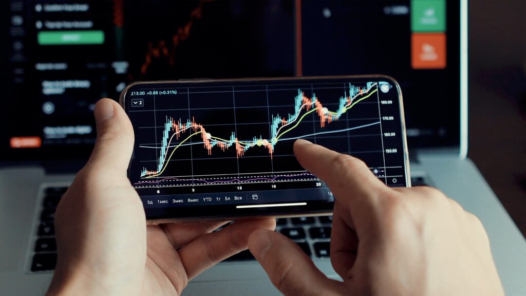 Man holding phone showing evolving Forex chart patterns and candlestick data.