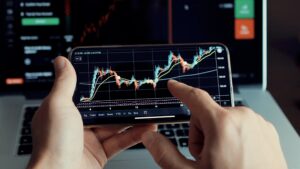 Man holding phone showing evolving Forex chart patterns and candlestick data.