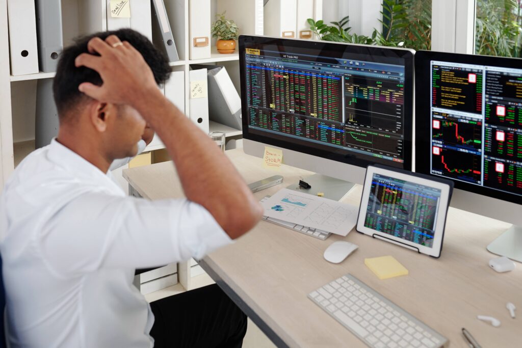 Stressed trader reacting to losses on multiple monitors due to FOMO in Trading