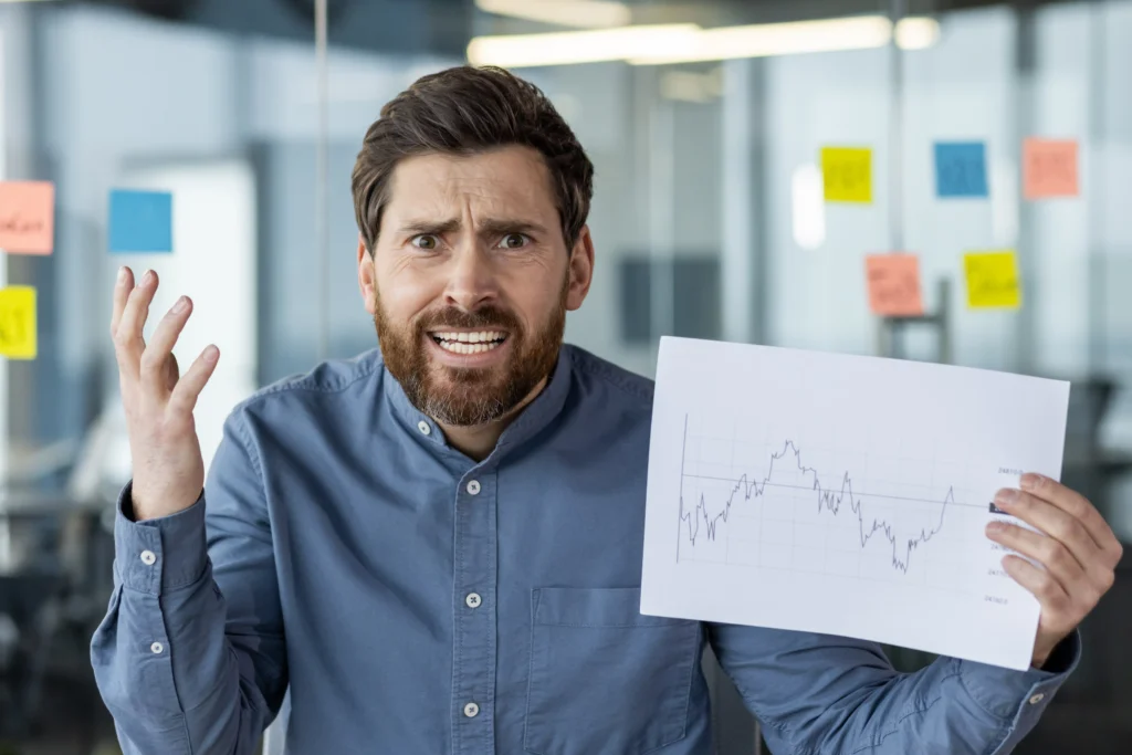 Frustrated trader showing chart with losses due to high leverage trading mistakes.