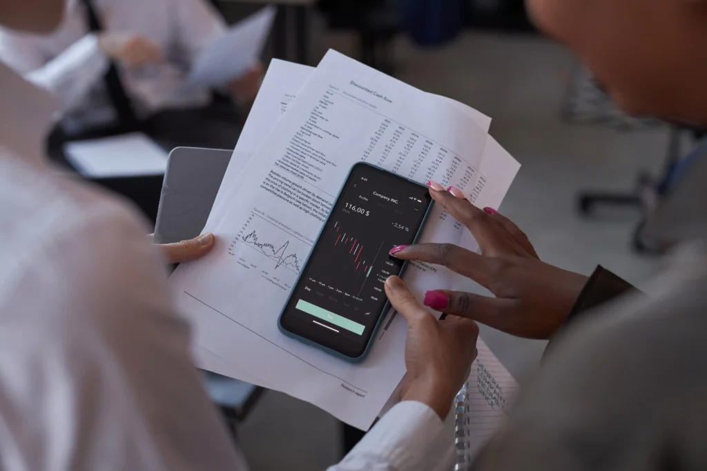 Slippage trading chart analysis on smartphone with printed financial reports.
