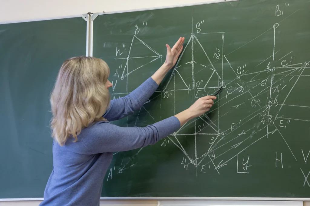 Teacher pointing at triangle chart pattern drawn on chalkboard with geometric and technical analysis details.