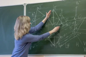 Teacher pointing at triangle chart pattern drawn on chalkboard with geometric and technical analysis details.
