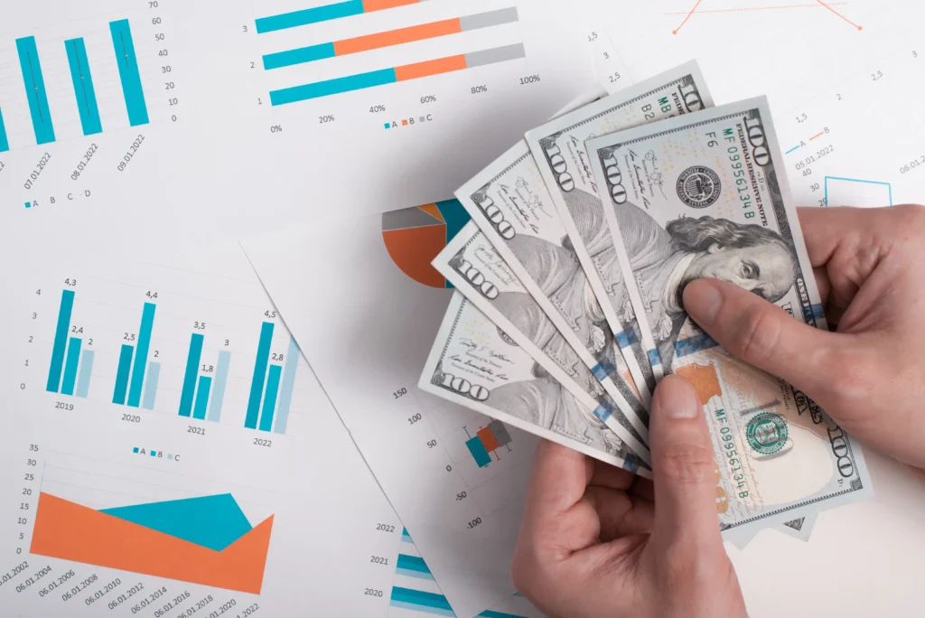 Hands holding cash above financial charts representing paper trading practice