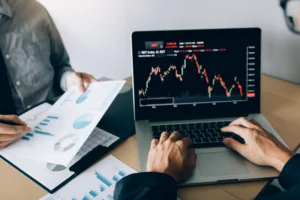 Traders comparing EMA vs SMA on laptop chart with financial documents, analyzing moving averages for trading strategy.