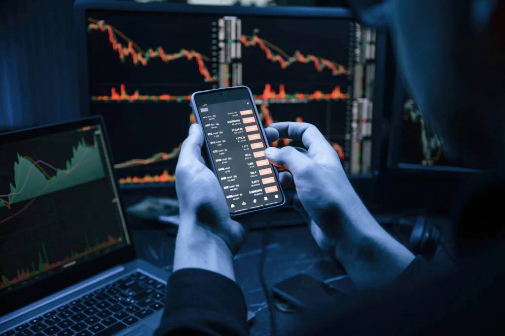 Person analyzing ROC Indicator on smartphone and computer screens with live market charts.