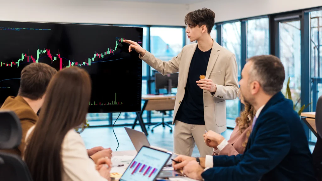 Business team learning breakout trading with a candlestick chart on a screen.