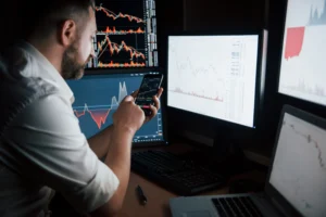 Trader analyzing charts on multiple screens and mobile phone while planning exit trading strategies for safer results