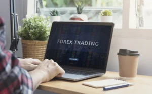 Person analyzing Forex Trading charts on a laptop with coffee cup and notebook on desk.