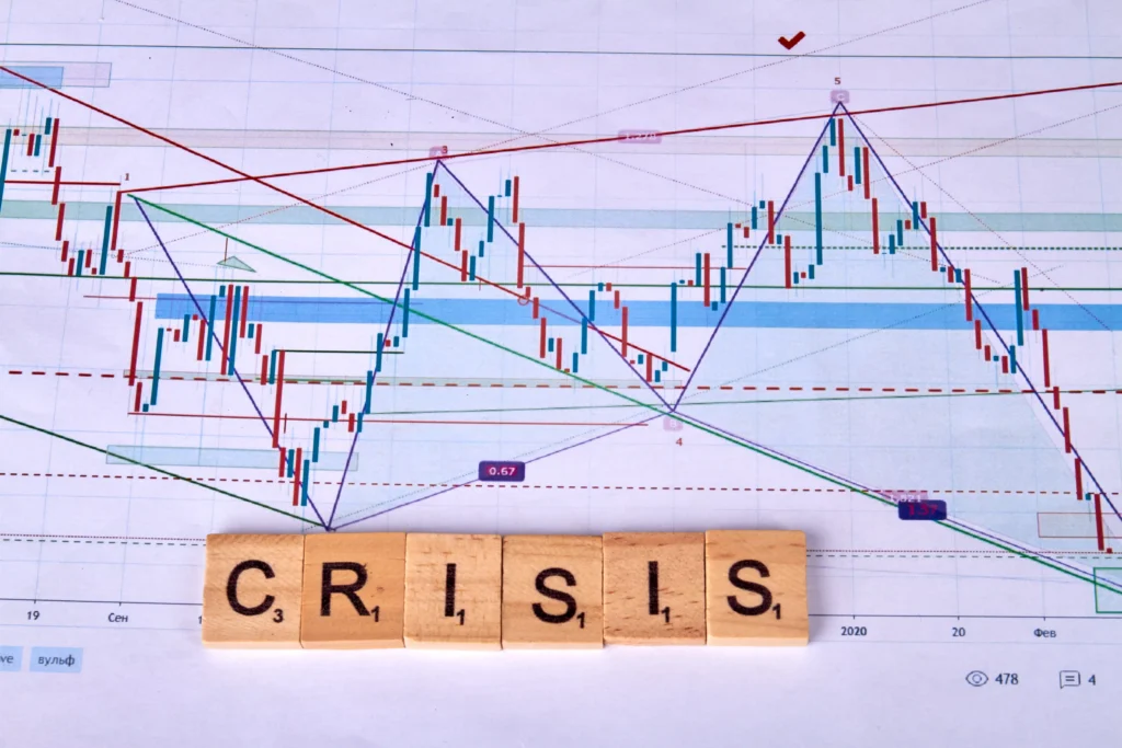 Crisis word on wooden blocks placed over a falling stock market candlestick chart representing market crash volatility.