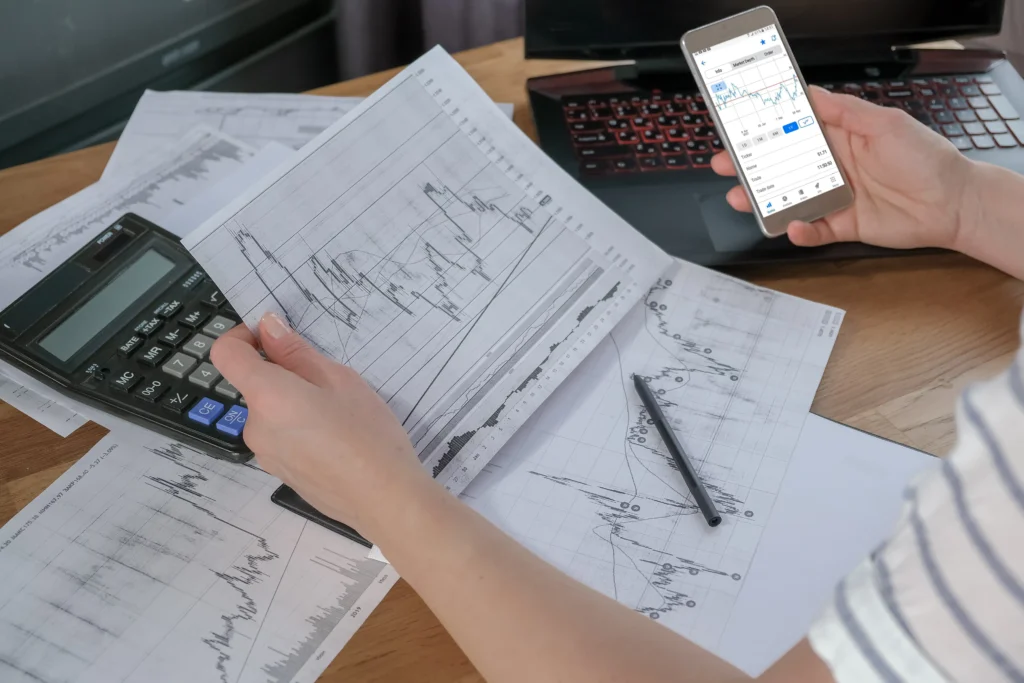 Person analyzing forex charts with calculator and mobile app for scalping with small account strategy.