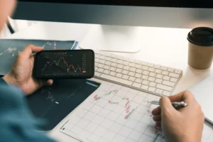 Trader reviewing charts with smartphone and paper, practicing best divergence trading strategy at a desk.