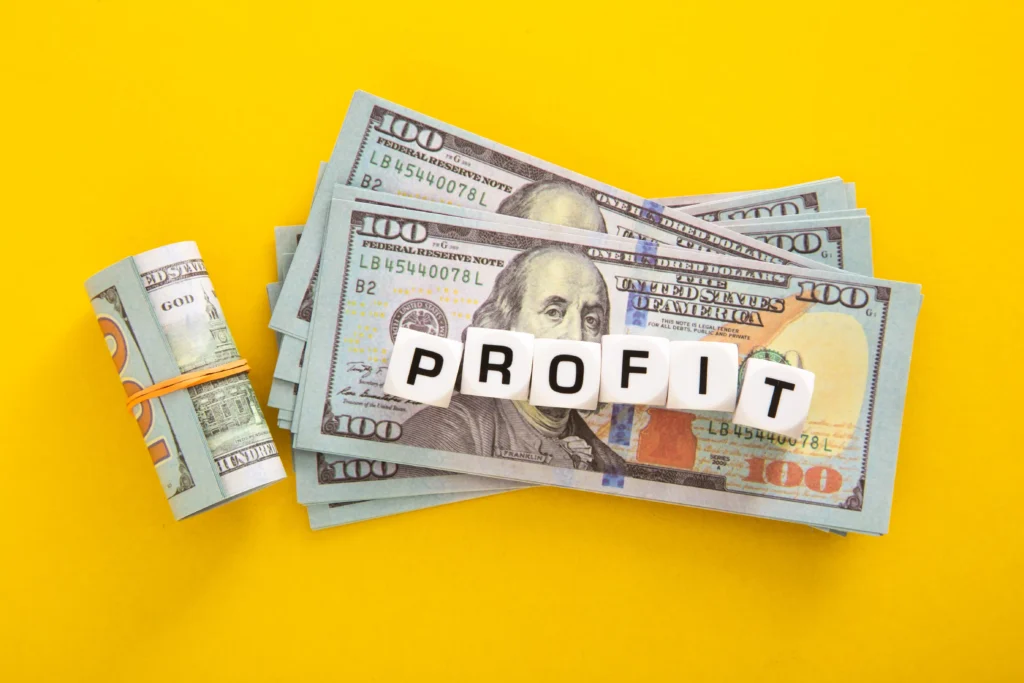 Stack of US dollar bills with profit word cubes on yellow background symbolizing consistent profits in trading