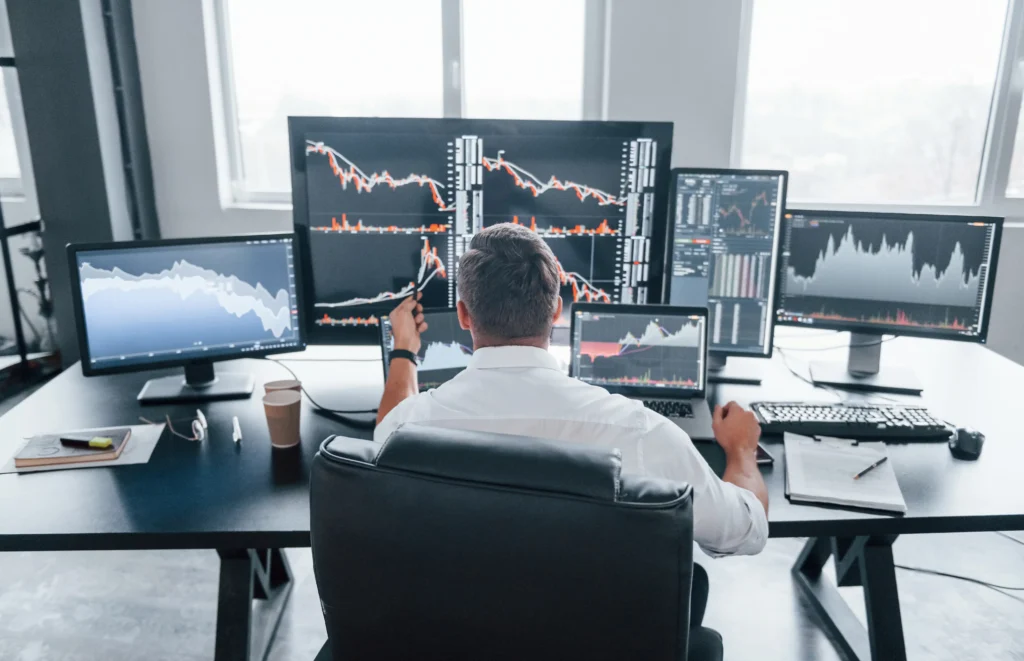 Trader analyzing charts and multiple monitors while applying backtesting trading strategies for accuracy in forex trading 2025
