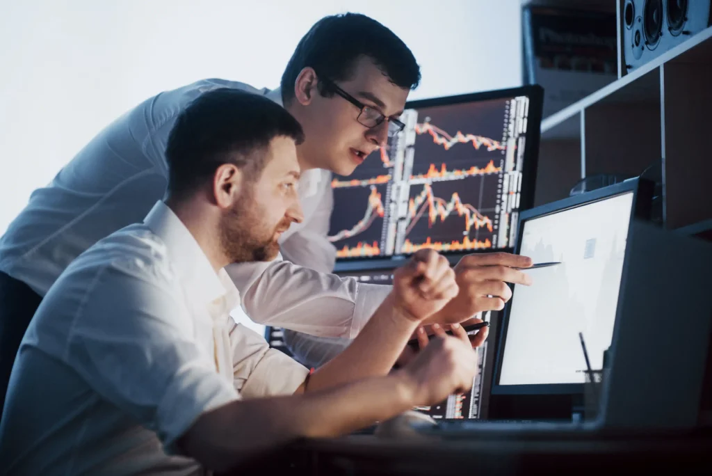 Two traders reviewing stock charts on multiple monitors while planning marginable securities trades in 2025.