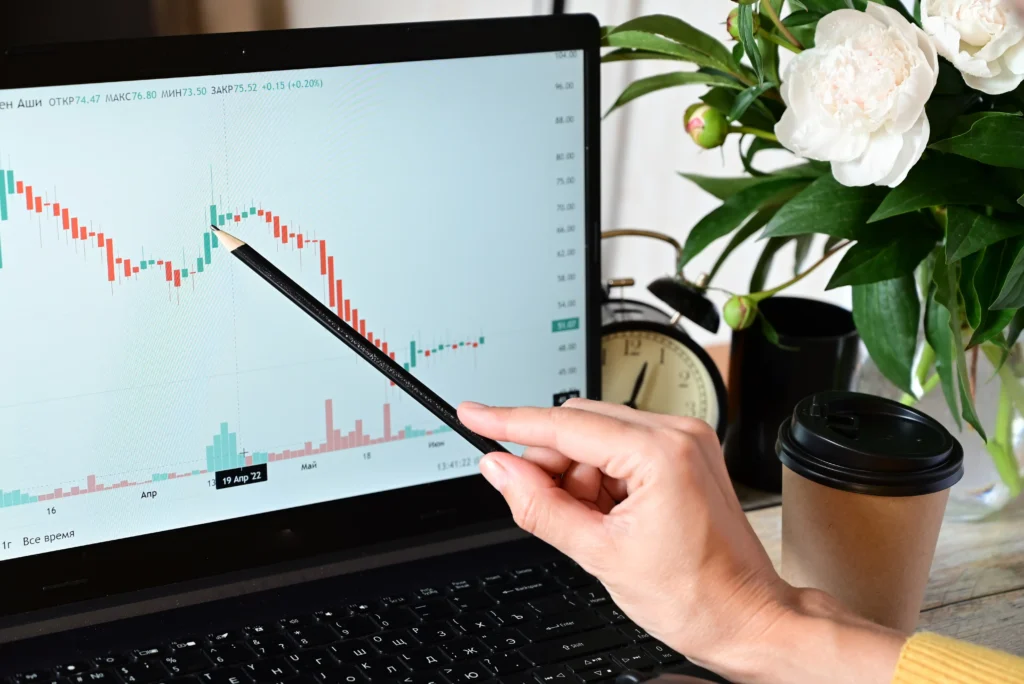 Trader using a pencil to highlight candlestick chart patterns on a laptop for compound trading analysis.