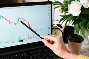 Trader using a pencil to highlight candlestick chart patterns on a laptop for compound trading analysis.