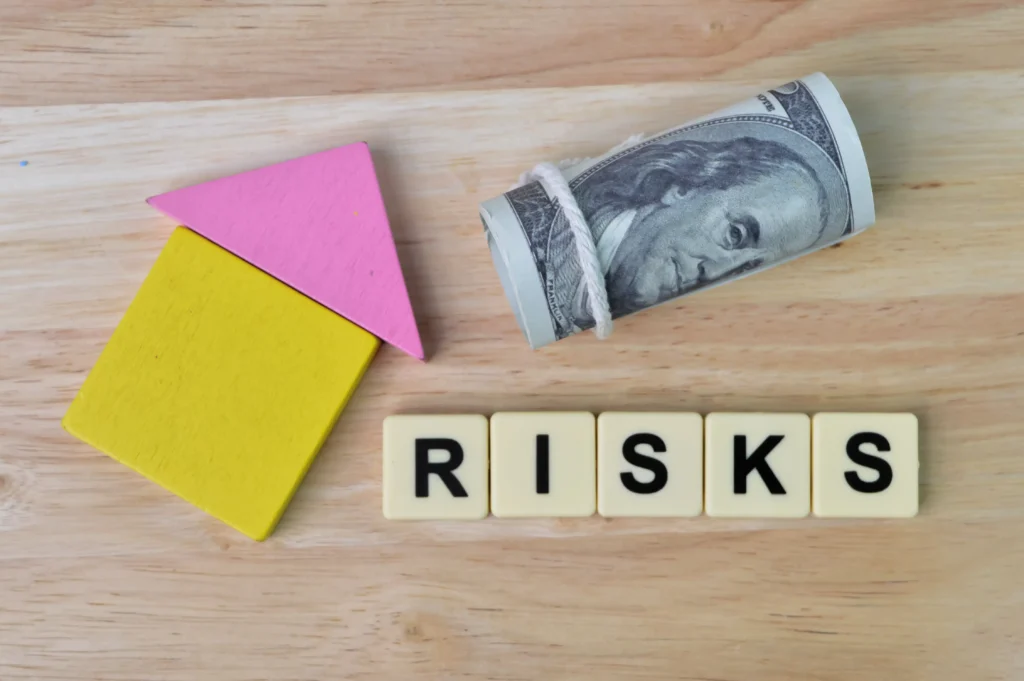 Wooden blocks shaped like a house, rolled US dollar bill, and the word risks spelled with tiles representing currency risk management.