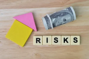 Wooden blocks shaped like a house, rolled US dollar bill, and the word risks spelled with tiles representing currency risk management.