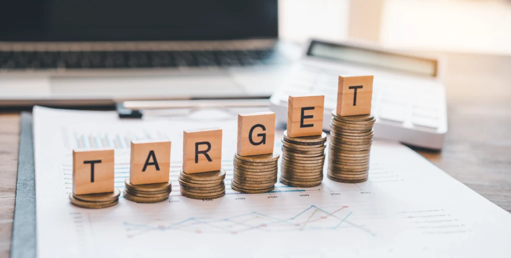 Price target calculation concept with wooden letter blocks on coin stacks for market prediction and financial planning 2025.