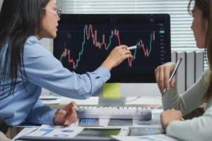 Two traders analyzing forex candlestick charts on a computer screen to discuss position sizing strategies