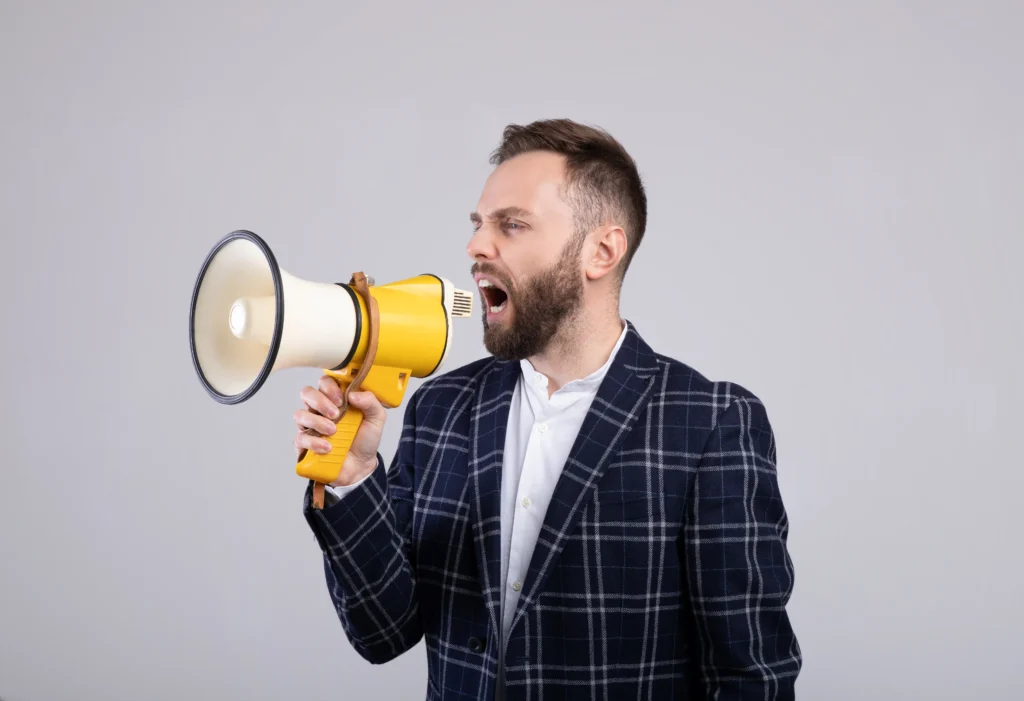 Man shouting through yellow megaphone symbolizing Megaphone Pattern Trading in 2025 financial markets.