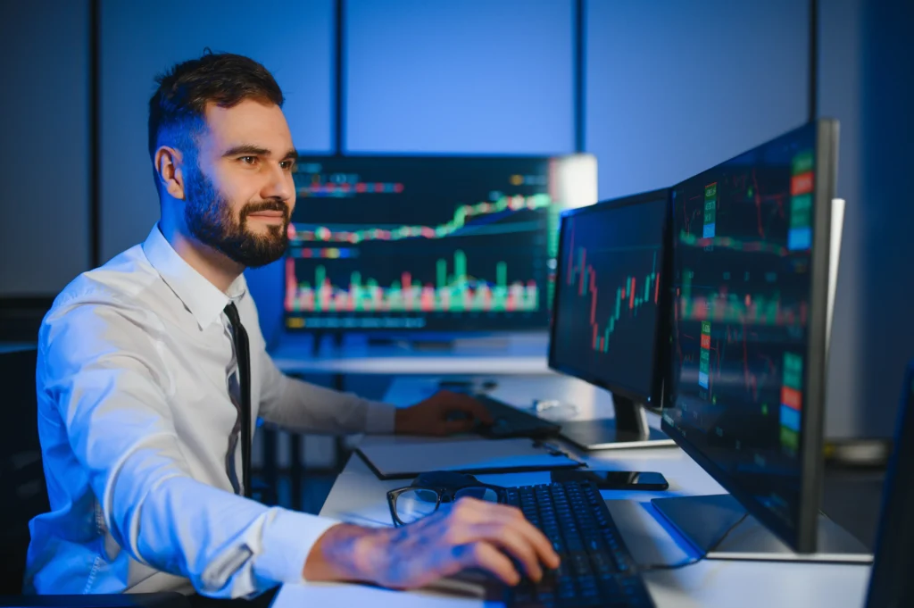 Trader analyzing multiple screens with candlestick charts and graphs, representing Algo Trading in 2025 with automated trading systems.
