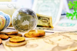 Glass globe on global map surrounded by US dollars and coins representing geopolitics in forex evolution in 2025.