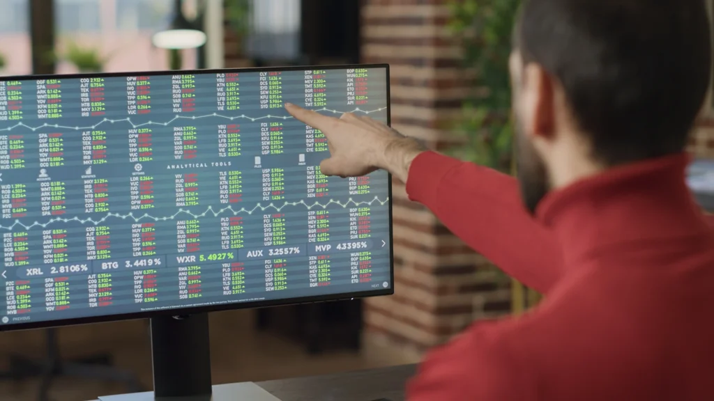 A trader pointing at live stock and forex order flow data on a computer screen for analysis.