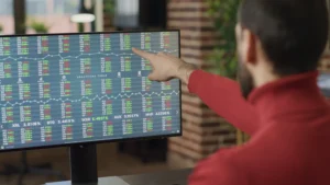 A trader pointing at live stock and forex order flow data on a computer screen for analysis.