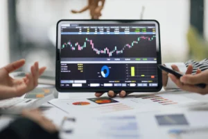 A tablet displaying forex candlestick charts and trading indicators during a financial analysis meeting.