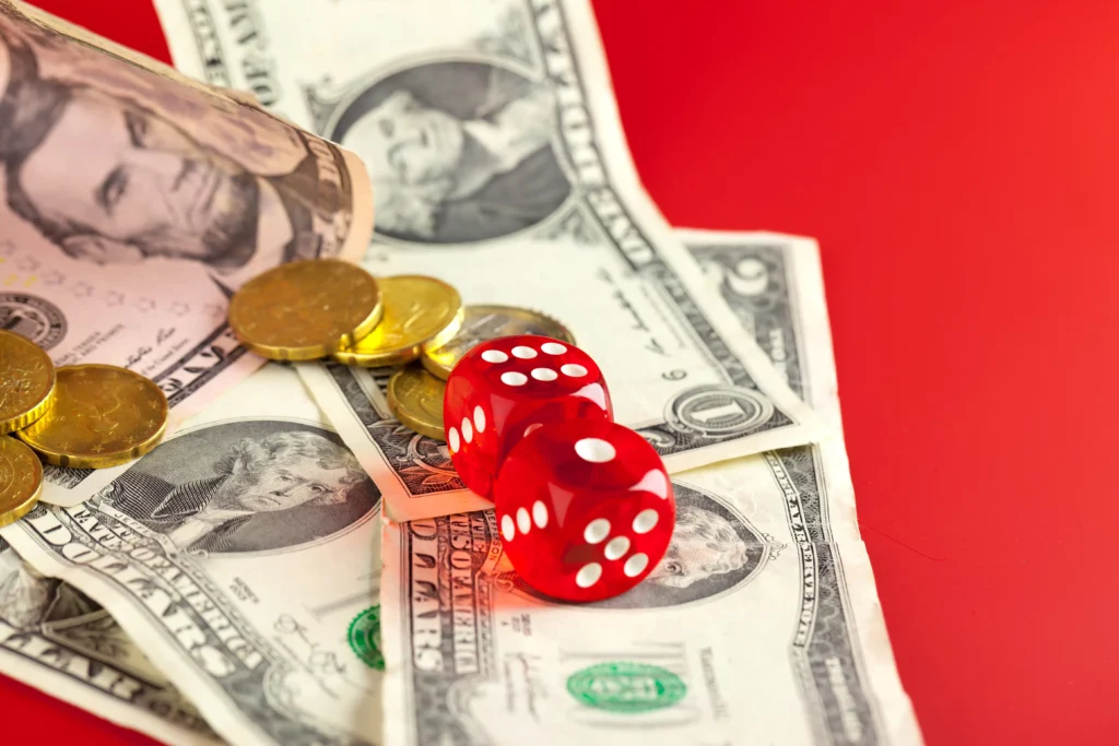 Red dice on U.S. dollar bills and coins representing the difference between trading and gambling with money risk.