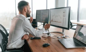 Man analyzing stock charts on dual monitors while discussing day trading tips for beginners in a modern office setting.
