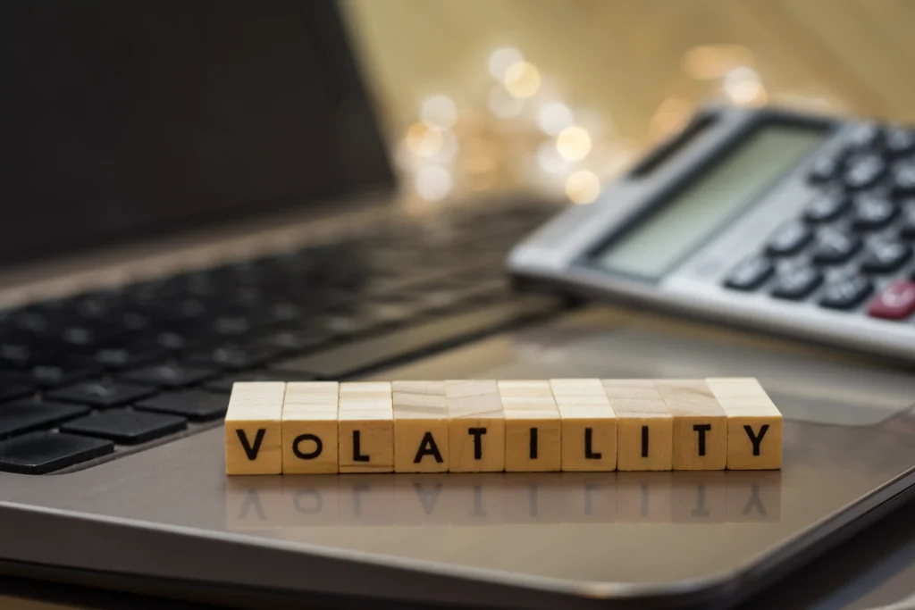 Wooden blocks spelling volatility on laptop with calculator symbolizing forex volatility indicators and financial risk measurement in 2025
