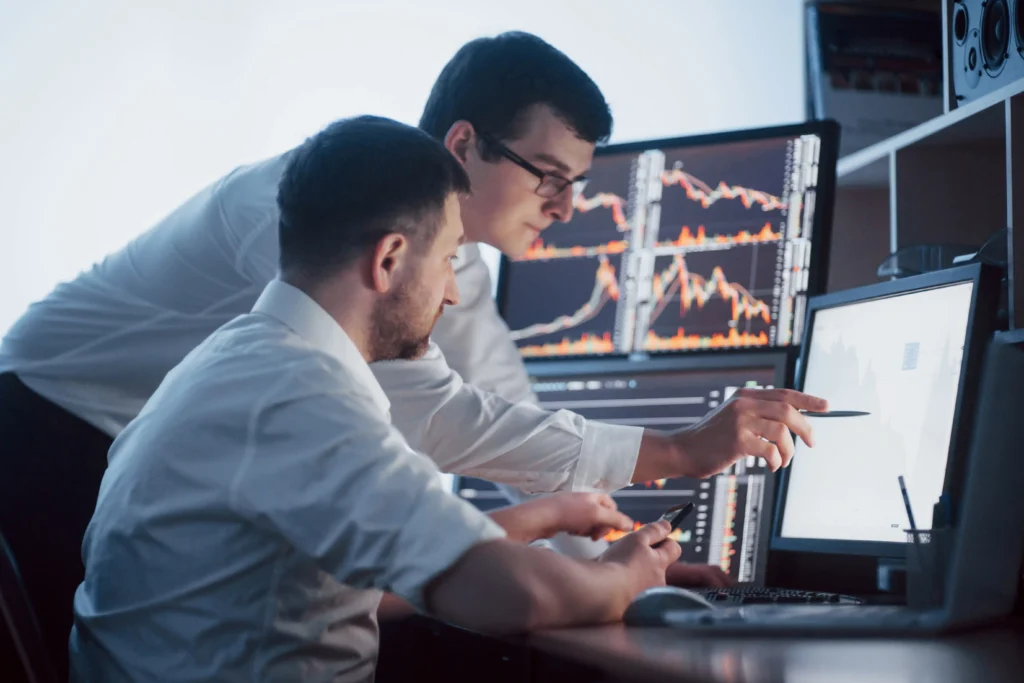 Two traders analyzing futures trading strategies 2025 on multiple computer screens with live market charts and financial data.