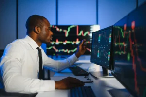Financial analyst monitoring algorithmic trading charts on multiple computer screens in a modern office.