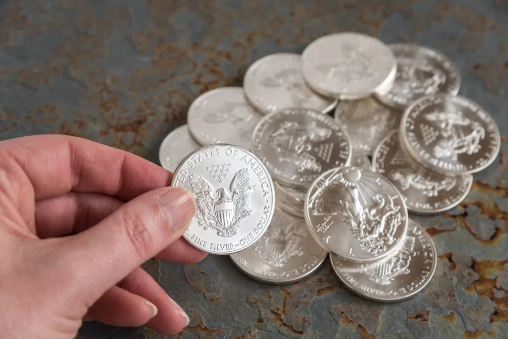 A person holding a U.S. silver dollar coin above a pile of silver coins, symbolizing silver investment and recent price volatility in 2025.