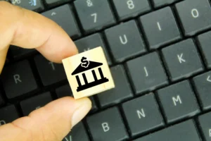 A hand holding a wooden block with a bank icon and dollar sign, symbolizing the rise of digital banking and Central Bank Digital Currencies (CBDCs).