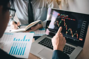 Two forex traders analyzing candlestick patterns and price charts on a laptop, discussing Break of Structure (BOS) and Market Structure Shift (MSS) trading strategy.