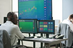 Trader analyzing multiple screens with live market data charts in a modern office environment representing Alternative Trading Systems (ATS) in action.