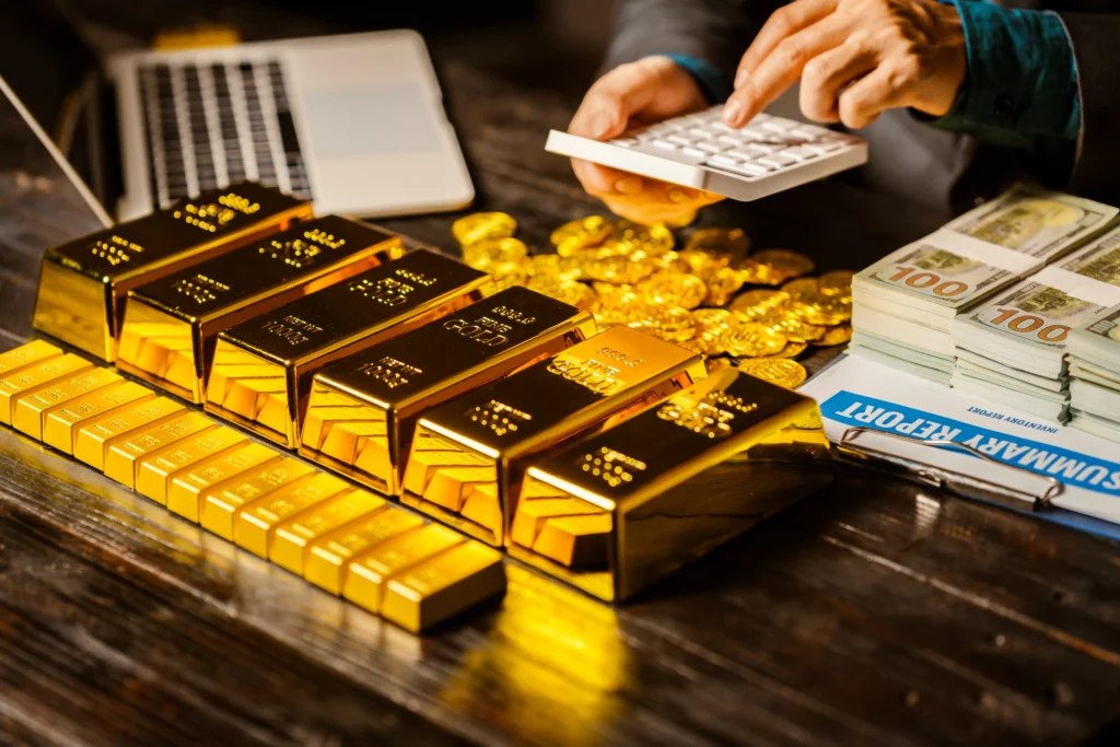 A person analyzing gold bars, gold coins, and cash stacks with a calculator while working on gold trading decisions.