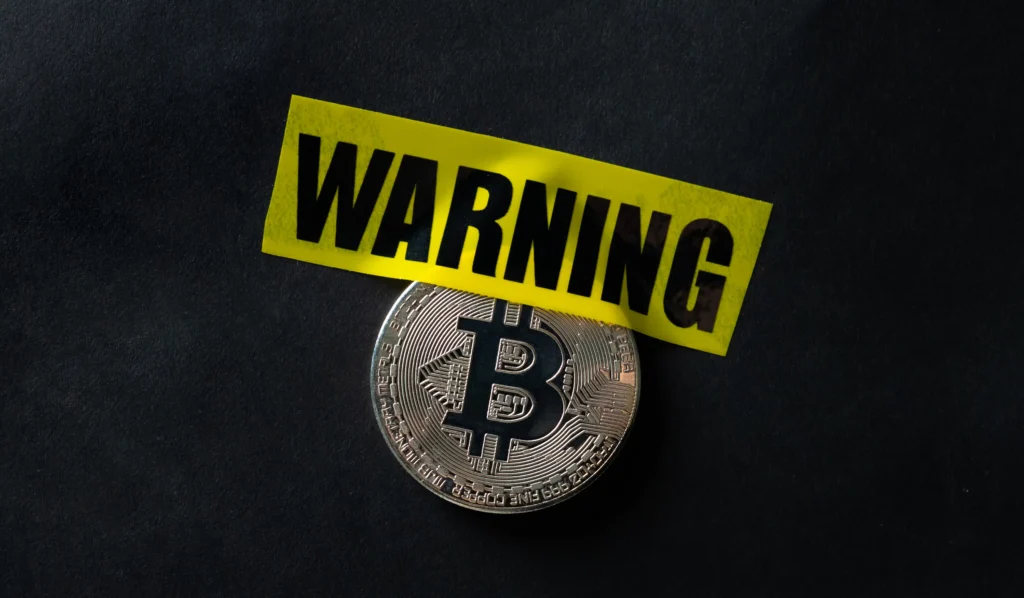 Bitcoin coin covered with yellow warning tape symbolizing awareness of Common Crypto Scams in 2025.